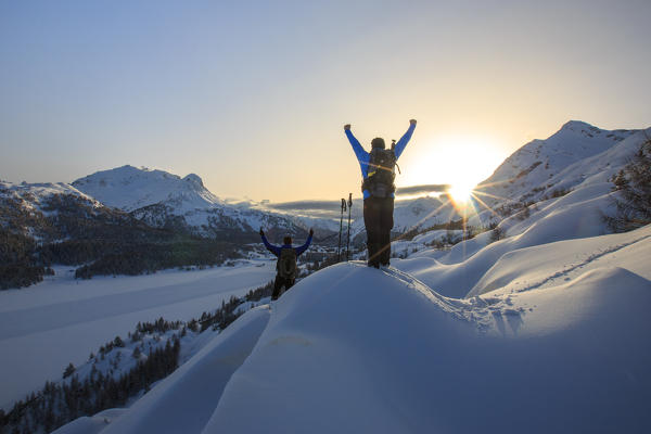 Snowshoe hikers rejoice backlit with view of Lake Sils. Maloja Pass. Engadine. Switzerland. Europe