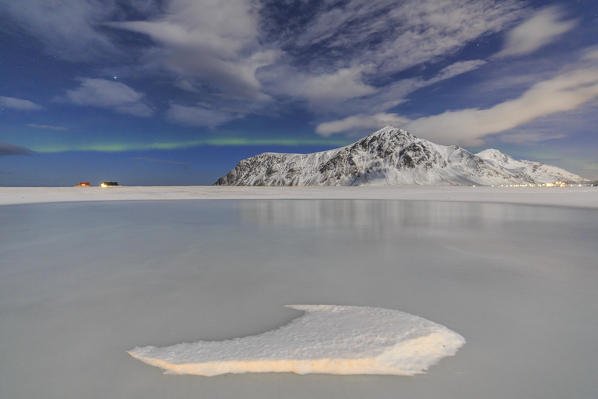 Northern Lights on the frozen sea and snow capped mountains. Flakstad Lofoten Islands Northern Norway Europe