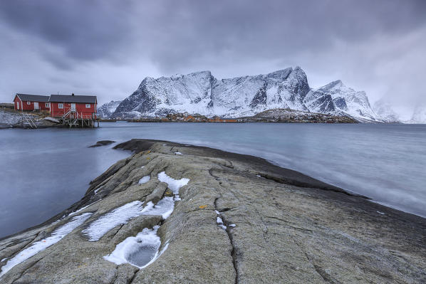 Typical red houses in the Hamnøy landscape with its cold sea and  snow capped peaks. Lofoten Islands Norway Europe