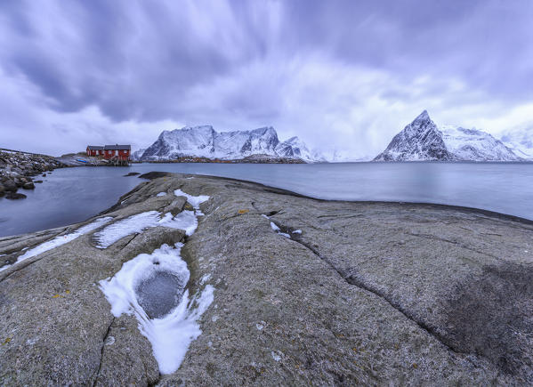 Typical red houses in Hamnøy landscape with its cold sea and  snow capped peaks. Lofoten Islands Norway Europe