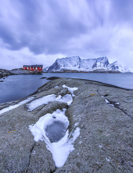 Typical red houses in the Hamnøy landscape with its cold sea and  snow capped peaks. Lofoten Islands Norway Europe