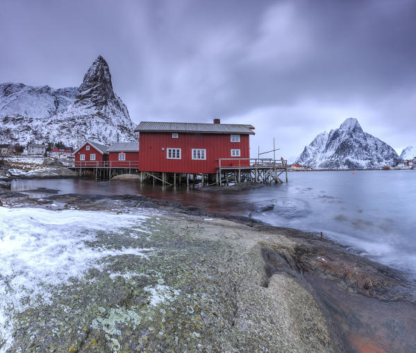 Typical red houses in Reine landscape with its cold sea and  snow capped peaks. Lofoten Islands Norway Europe