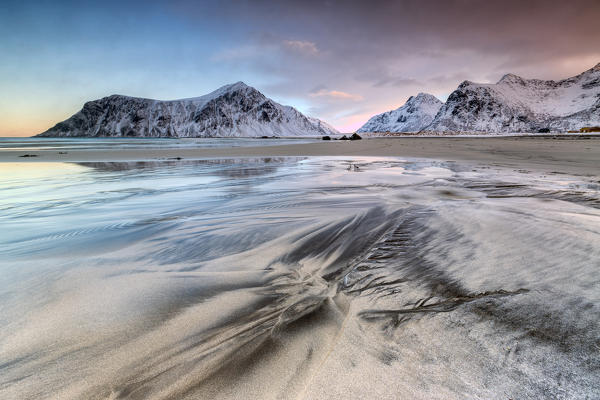 Pink sky on the  surreal Skagsanden beach surrounded by snow covered mountains.  Lofoten Islands Northern Norway Europe