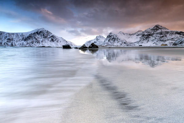 Pink sky on the  surreal Skagsanden beach surrounded by snow covered mountains.  Lofoten Islands Northern Norway Europe