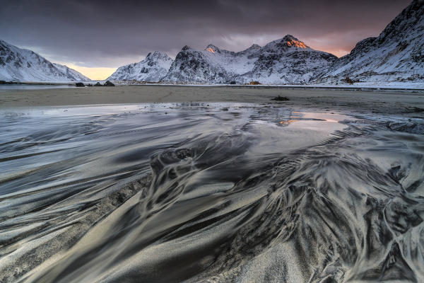 Waves on the  surreal Skagsanden beach surrounded by snow covered mountains. Lofoten Islands Norway. Europe