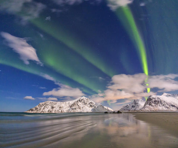 Northern Lights illuminate Skagsanden beach and the snowy peaks. Lofoten Islands Northern Norway Europe