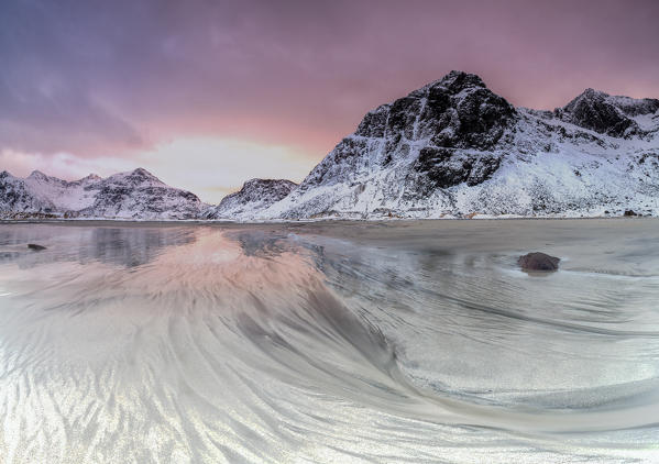 Pink sky on the  surreal Skagsanden beach surrounded by snow covered mountains. Lofoten Islands Northern Norway Europe