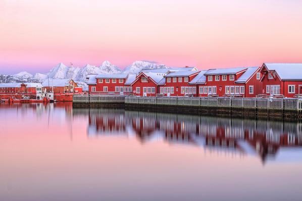 Pink sunset over the typical red houses reflected in the sea. Svollvaer Lofoten Islands Norway Europe