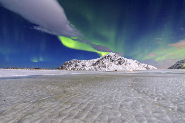 Northern Lights illuminate the sky and the snowy peaks. Flakstad. Lofoten Islands Northern Norway Europe