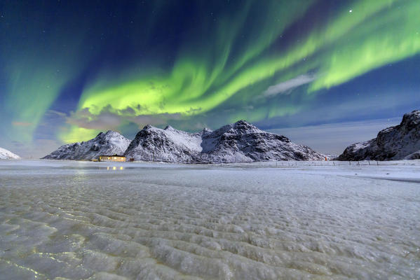 Northern Lights illuminate the sky and the snowy peaks. Flakstad. Lofoten Islands Northern Norway Europe