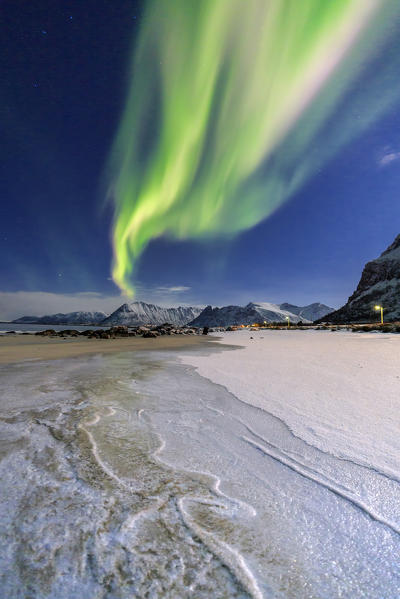 The aurora borealis lights up the sky and the beach of the cold sea of Gymsøyand. Lofoten Islands Northern Norway Europe