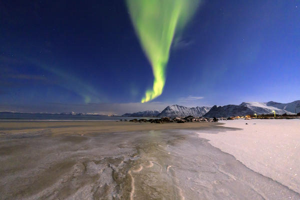 The aurora borealis lights up the sky and the beach of the cold sea of Gymsøyand. Lofoten Islands Northern Norway Europe