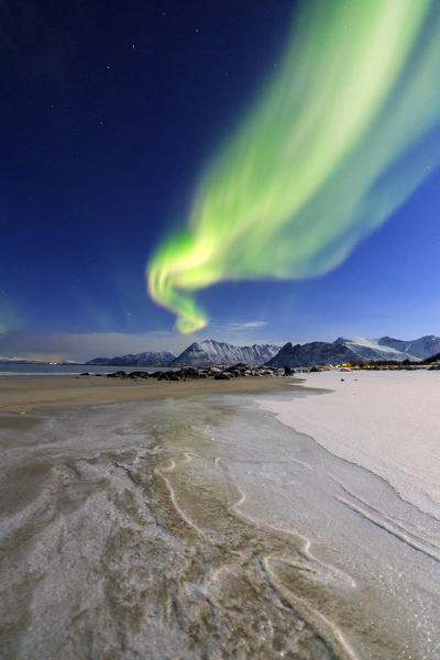 The aurora borealis lights up the sky and the beach of the cold sea of Gymsøyand. Lofoten Islands Northern Norway Europe