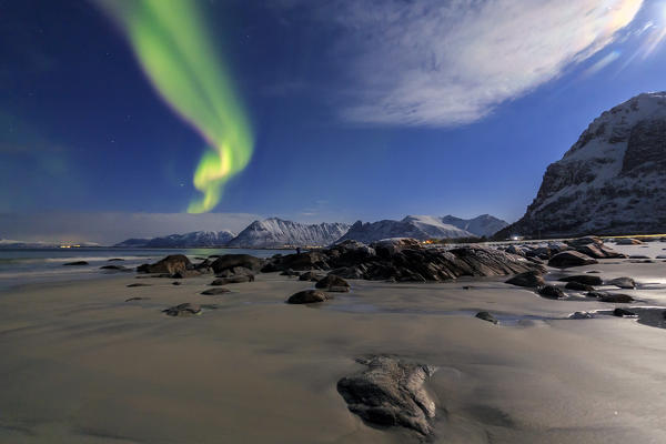 The aurora borealis lights up the sky and the beach of the cold sea of Gymsøyand. Lofoten Islands Northern Norway Europe