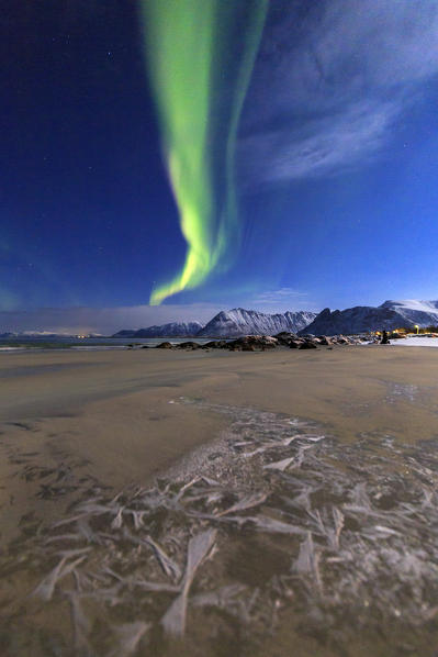 The aurora borealis lights up the sky and the beach of the cold sea of Gymsøyand. Lofoten Islands Northern Norway Europe