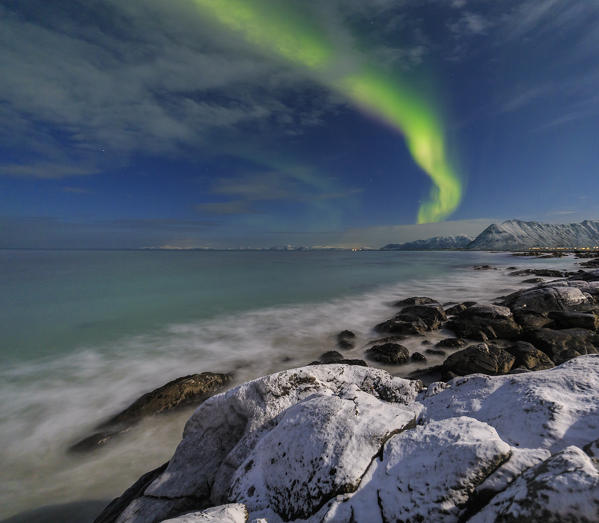 Northern lights on the cold sea of  Gymsøyand where the waves break on the rocks. Lofoten Islands Northern Norway Europe