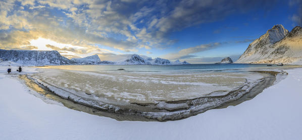 Hiker admire the golden sunrise over a strip of land where the snow has melted. Haukland Lofoten Islands Norway Europe