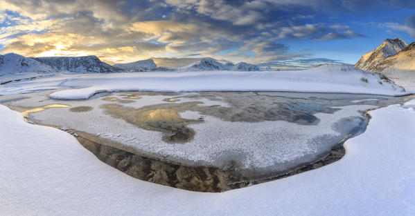 The golden sunrise reflected in a pool of the clear sea where the snow is almost melted. Haukland Lofoten Islands Norway Europe