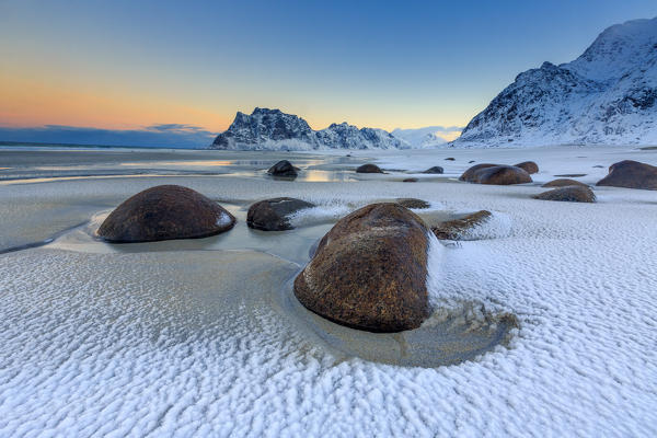 Dawn illuminates the rocks shaped by wind surrounded by fresh snow. Uttakleiv Lofoten Islands Norway Europe