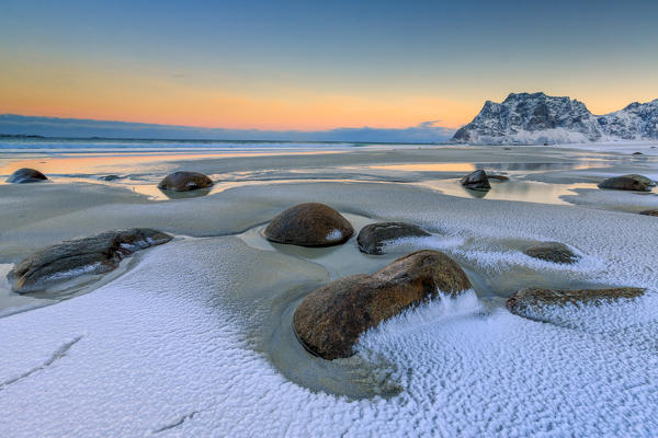 Dawn illuminates the rocks shaped by wind surrounded by fresh snow. Uttakleiv Lofoten Islands Norway Europe