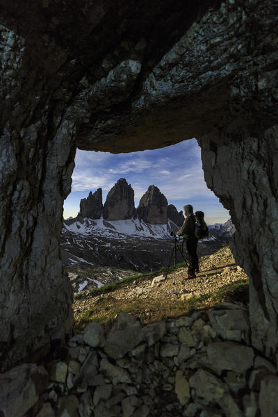 Hiker admires  the Three Peaks of Lavaredo out of a cave at night. Sesto Dolomites Trentino Alto Adige Italy