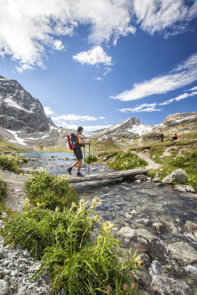 Hiker crossing a stream Engadine Canton of Grisons Switzerland Europe