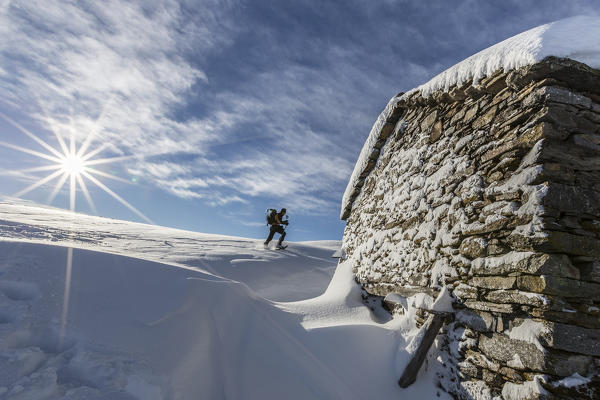 Snowshoe hiker walking near snow covered hut  Motta di Olano Gerola Valley Valtellina Orobie Alps Lombardy Italy Europe