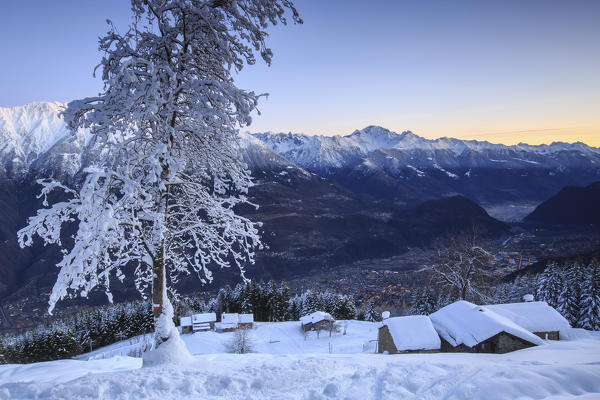 Lights of dusk illuminate the valley and the snow covered huts Tagliate Di Sopra Gerola Valley Valtellina Lombardy Italy Europe