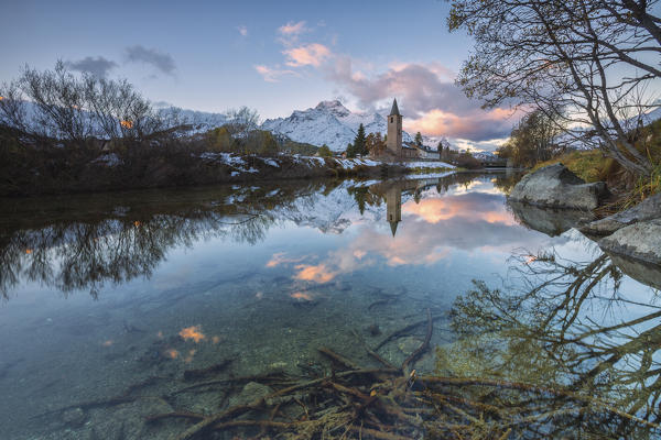 Dawn illuminates the snowy peaks and the bell tower reflected in Lake Sils Engadine Canton of Graubünden Switzerland Europe