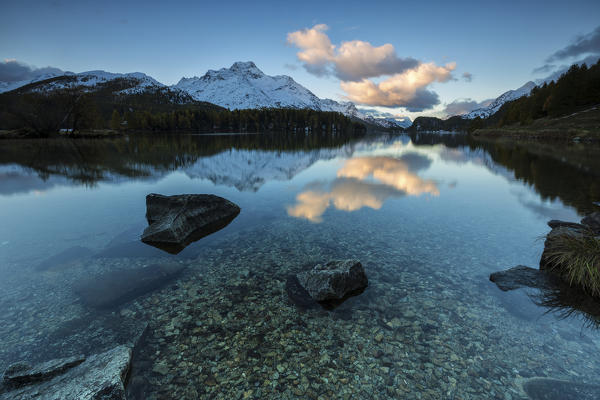 Dawn illuminates the peaks reflected in the calm waters of Lake Sils Engadine Canton of Graubünden Switzerland Europe
