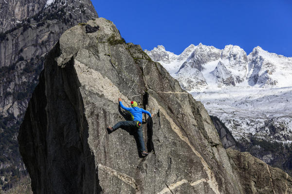 Climber on steep rock face in the background blue sky and snowy peaks of the alps Masino Valley Valtellina Lombardy Italy Europe