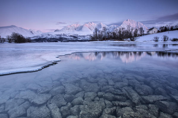 Snowy peaks are reflected in the frozen Lake Jaegervatnet at sunset Stortind Lyngen Alps Tromsø Lapland Norway Europe