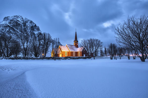 The illuminated church at dusk in the cold snowy landscape at Flakstad Lofoten Norway Europe