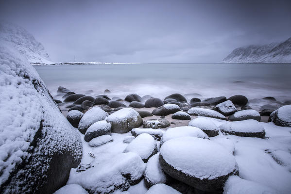 Snow covered rocks on the beach modeled by the wind surround the icy sea Pollen Vareid Flakstad Lofoten Islands Norway Europe