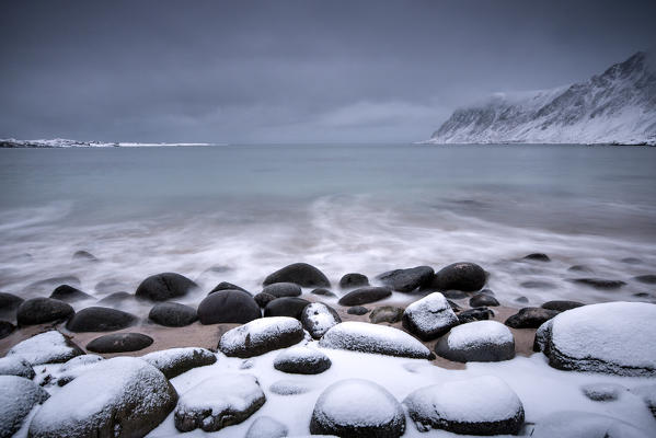 Snow covered rocks on the beach modeled by the wind surround the icy sea Pollen Vareid Flakstad Lofoten Islands Norway Europe