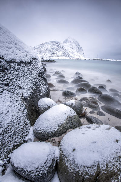 Snow covered rocks on the beach modeled by the wind surround the icy sea Pollen Vareid Flakstad Lofoten Islands Norway Europe