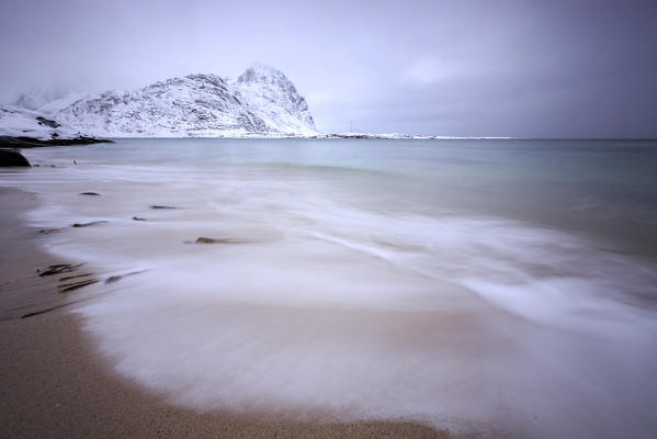 Waves of the icy sea on the beach in the background the snowy peaks Pollen Vareid Flakstad Lofoten Islands Norway Europe