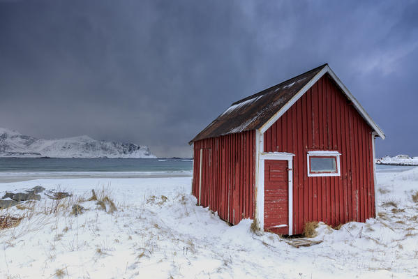 A typical house of the fishermen called rorbu on the snowy beach frames the icy sea at Ramberg Lofoten Islands Norway Europe