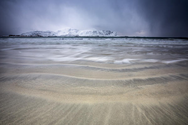 Waves of the icy sea on the beach in the background the snowy peaks Ramberg Lofoten Islands Norway Europe