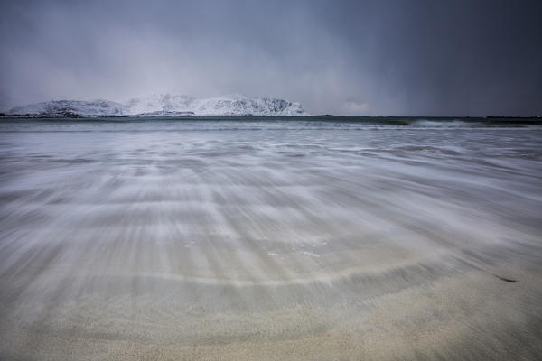 Waves of the icy sea on the beach in the background the snowy peaks Ramberg Lofoten Islands Norway Europe