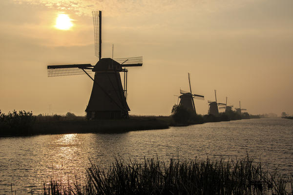 Morning sun just risen shines in the canal where windmills are reflected Kinderdijk Rotterdam South Holland Netherlands Europe