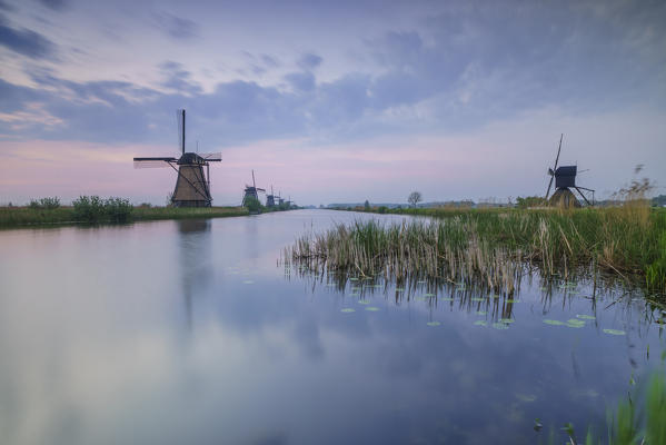 Blue sky and pink clouds on the windmills reflected in the canal at dawn Kinderdijk Rotterdam South Holland Netherlands Europe