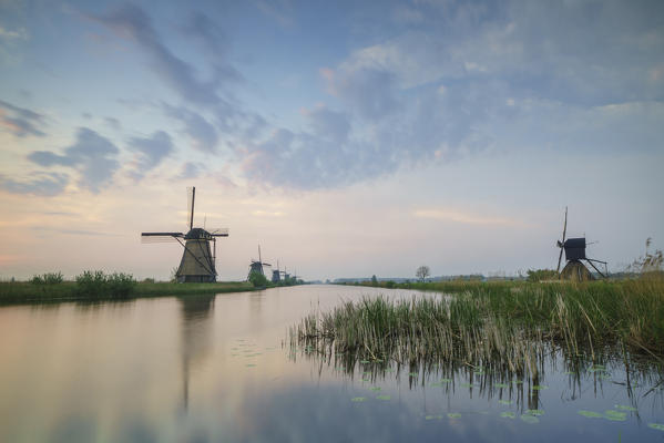 Blue sky and pink clouds on the windmills reflected in the canal at dawn Kinderdijk Rotterdam South Holland Netherlands Europe