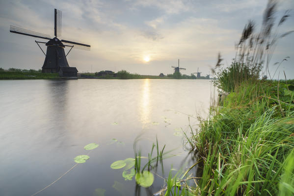 Morning sun just risen shines in the canal where windmills are reflected Kinderdijk Rotterdam South Holland Netherlands Europe