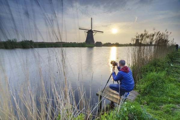 Photographer in action shooting the windmill reflected in the canal Kinderdijk Rotterdam South Holland Netherlands Europe