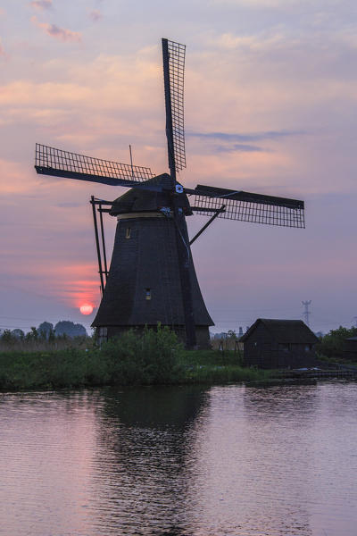 Pink sky at sunrise on the windmill reflected in the canal Kinderdijk Rotterdam South Holland Netherlands Europe