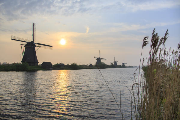 Morning sun just risen shines in the canal where windmills are reflected Kinderdijk Rotterdam South Holland Netherlands Europe