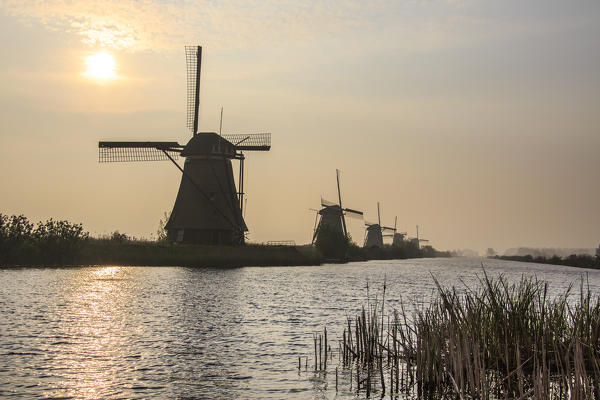 Morning sun just risen shines in the canal where windmills are reflected Kinderdijk Rotterdam South Holland Netherlands Europe