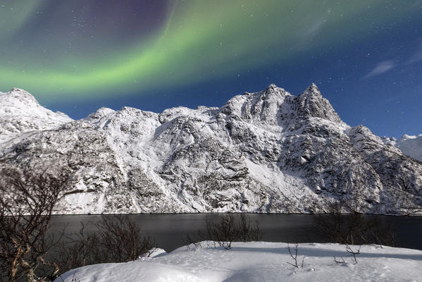 Northern Lights illuminate the snowy peaks and the blue sky during a starry night Budalen Svolvaer Lofoten Islands Norway Europe