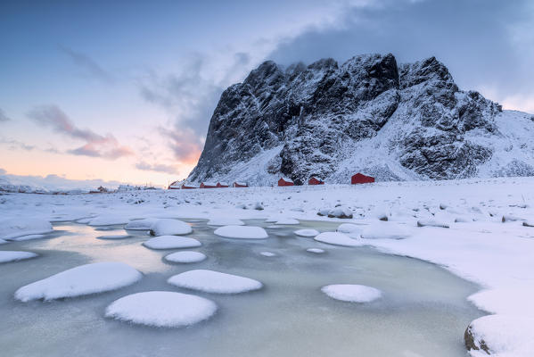 Snowy peaks and ice frame the typical fishermen houses called Rorbu Eggum Vestvagøy Island Lofoten Islands Norway Europe